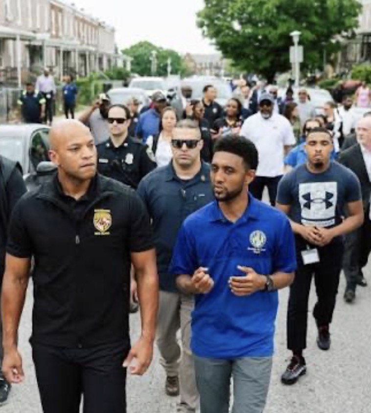 A diverse group of people, including law enforcement officers and community members, walking together on a street, engaging in dialogue during a community event.